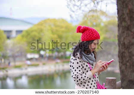 beautiful young woman with maroon beanie hat using smartphone smiling outdoors in park in spring.