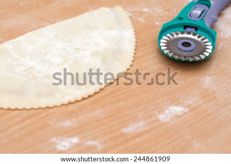 raw pie with wavy edge tool for cutting pizza on the kitchen table