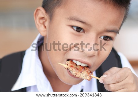 Portrait of little boy eating grilled pork.