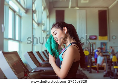 Attractive asian girl running on the treadmill in the gym with towel after training