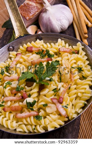 Cooked spiral macaroni on a old pan with bacon, garlic and bread sticks, on a wood and bamboo mat
