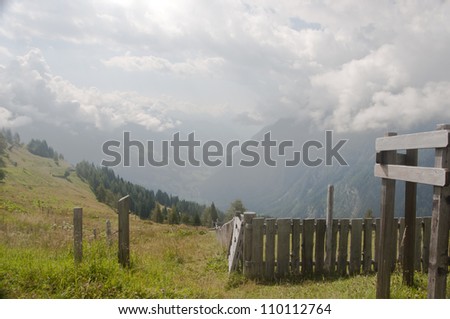 A view onto Austrian Alps: hills with meadows and fence in the front