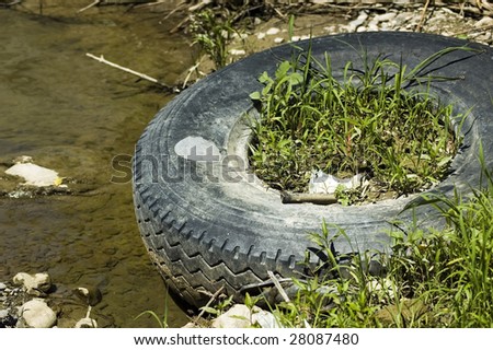 Trash and waste in the river, rubber tire in the mud