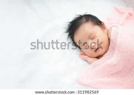 Cute newborn asian girl sleeping on furry cloth wearing roses headband