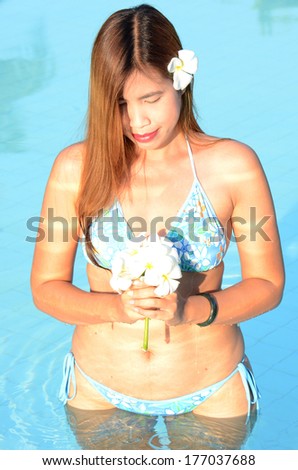 Long hairs beautiful lady in swimming pool and white flowers in her hand