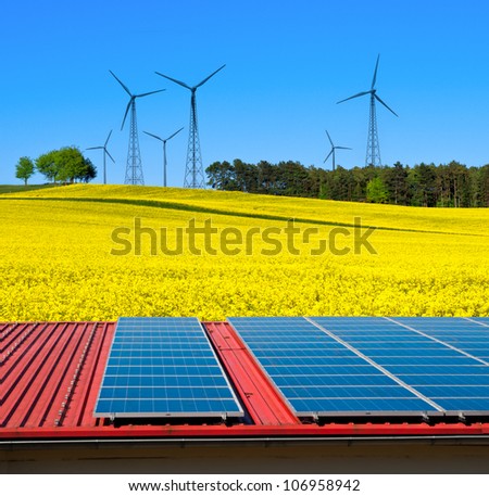 Solar power cells on a barn roof with a view over rapeseed field with windmills on the horizon