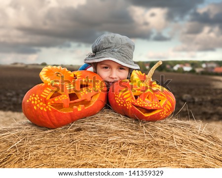 Little boy with two carved halloween pumpkins on a roll of hay
