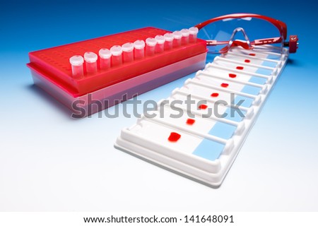 Tube stand full of samples, protective glasses and tray with blood samples on blue gradient background
