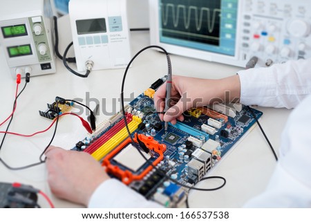 Female Tech tests electronic equipment in service centre. Tilt-shift, shallow DOF, focus on the instrument in right hand