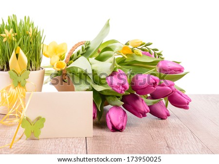 Spring flower arrangement and a greeting card on a wooden table against white wall, text space