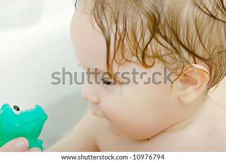 seven month old baby-boy in a bath tub looking at green crocodile toy