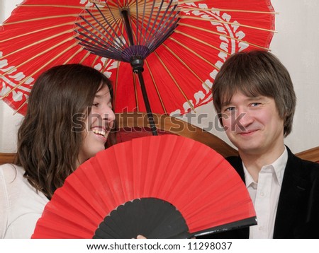 playful couple sitting on a couch holding red fan and red umbrella