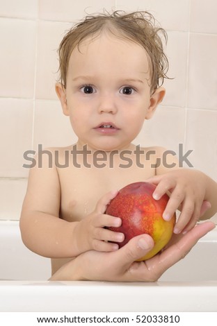 a one year old boy stands in a bath tub taking a peach from his mama\'s hand