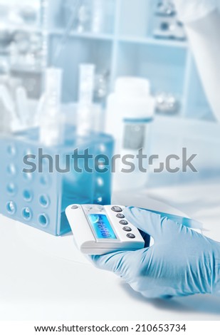 Scientific background with gloved hand holding electronic timer as a focal point, tilt-shift effect,  text space