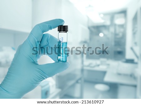 Gloved hand holds a liquid sample in plastic tube, lab out of focus, text space