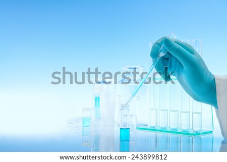 Scientific background with chemical glass, flask, tubes and gloved hand loading sample