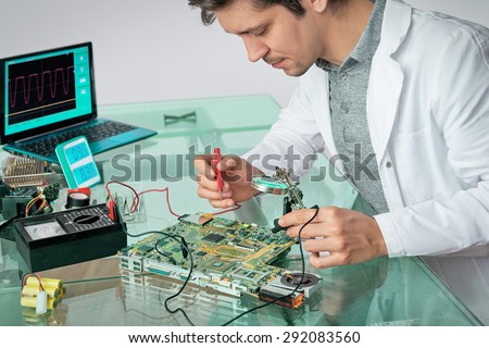 Young energetic male tech fixes laptop motherboard, shallow DOF, focus on the eyelashes