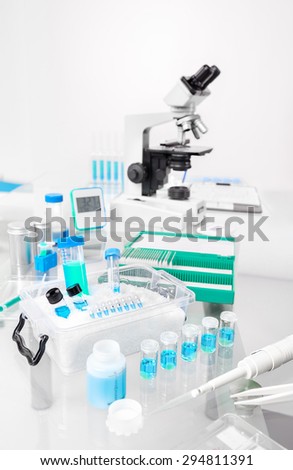 Scientific background with samples, pipette, ice basket and microscope in gray and blue. Focus on the blue samples in front. Space for your text on the top
