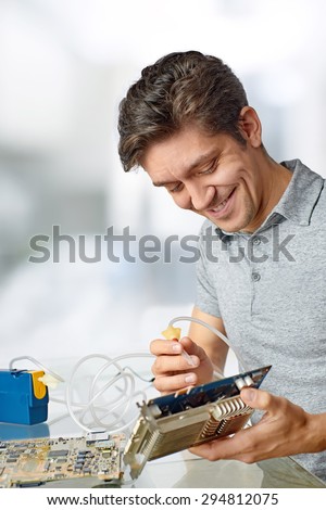Smiling male tech cleans faulty computer processor in hardware repair workshop