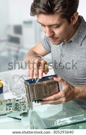 Young male tech cleans faulty computer processor in hardware repair workshop. Focus on the face and fingers
