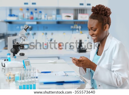 African-american biologist in the lab texting someone on her mobile with a smile
