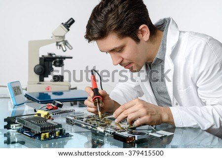 Young energetic male tech or engineer repairs electronic equipment in research facility. Shallow DOF, focus on the face and hands of the worker.