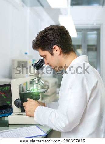 Male scientist or tech with dark hair and brown eyes works with microscope samples in research facility
