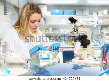 Young female tech or scientist loads liquid sample into test tube with plastic pipette. Shallow DOF, focus on the eyelashes and hand with the tubes.