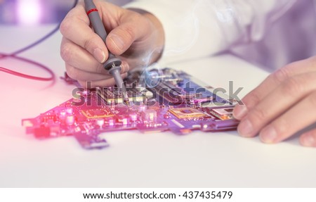 Electronics repair service, hands of female tech fixes an electronic circuit. Shallow DOF, focus on the tip of the test device and part of the hand. This image is toned.