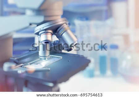 Scientific background with closeup on light microscope and laboratory out of focus. This image is toned. Shallow DOF, focus on the slide glass.