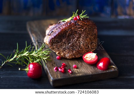 baked meat with rosemary and red pepper. steak. beef. dinner for men. dark photo. Black background. wooden board.