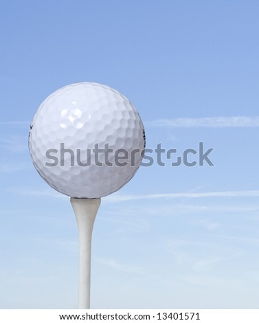 A closeup of a golf ball on a tee a blue sky background.
