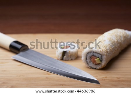 Sushi sits on a bamboo cutting board with a knife.