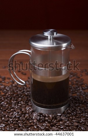 A coffee press is surrounded by coffee beans