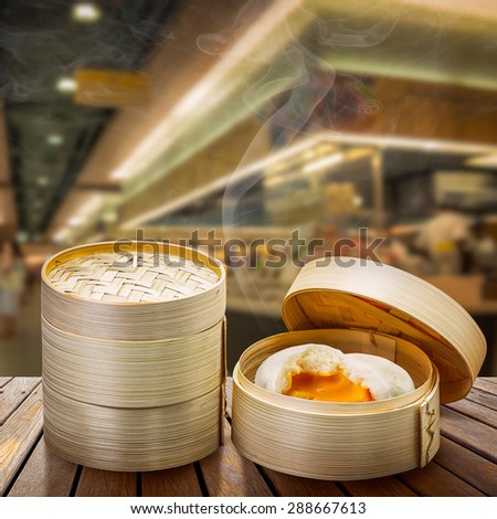 Chinese steamed bun and sweet creamy stuff in bamboo ware on wooden table at restaurant