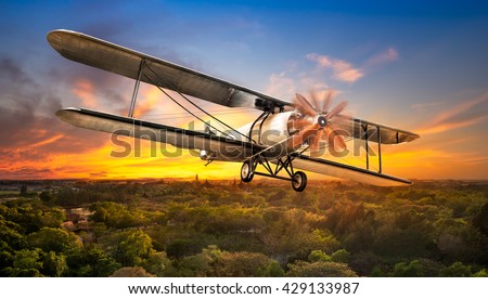 Ancient airplane flying over the rural scene on sunset background