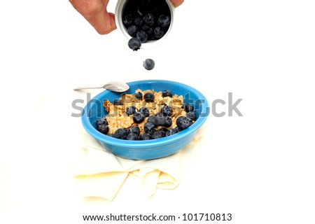 A blue bowl of cereal with fresh blueberries poured over the top.