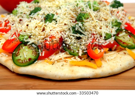 A veggie pizza ready to go into the oven topped with sharp cheddar and asiago cheese, fresh tomatoes, red bell pepper, mild jalapeno chilie, broccoli and dried herbs