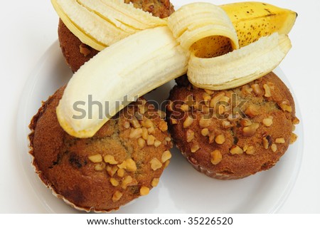 Closeup of three banana nut muffins topped with crushed walnuts with a fresh pealed banana