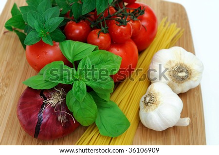 Fresh herbs and vegetables to make spaghetti, including red onion, tomatoes, basil, oregano, garlic and dry pasta.