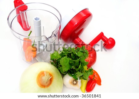 Hand powered food processor with all the ingredients to make a mexican salsa including onion, cilantro, garlic, chili and tomato