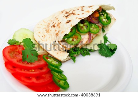 Pita bread sandwich with lettuce, swiss cheese, grilled onions and jalapeno pepper, tomatoes, cucumber on a white plate