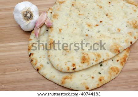 Garlic flavored East Indian Naan flat bread with fresh garlic cloves on a wooden cutting board