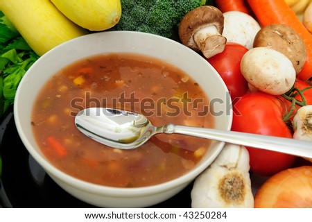 Bowl of veggie soup with a spoon surround by assorted fresh vegetables