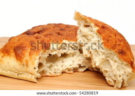 A square loaf of artisan bread with a corner of the loaf torn off on a wooden cutting board