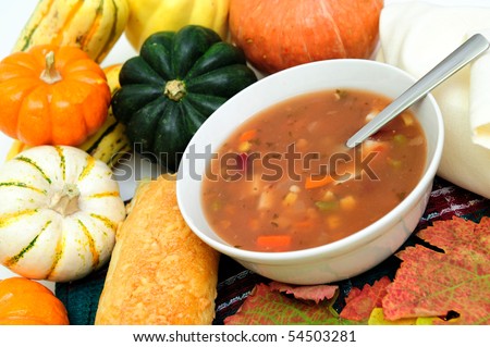 a bowl of warm veggie soup with seasonal Autumn vegetables and colorful fall leaves