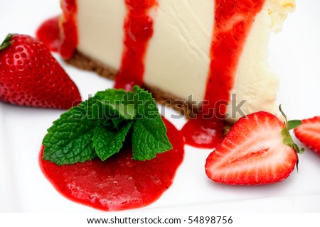 Slice of cheesecake with fresh strawberries and and a bright red strawberry sauce dripping over the sides on the dessert.
