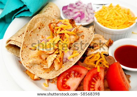 Spicy white meat chicken taco with red onion, cheddar cheese, sliced tomatoes and a small bowl of red hot sauce