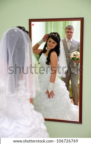 The bride corrects hairdresses and looks in a mirror. Groom behind