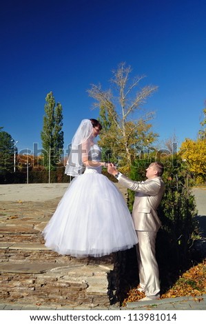 The groom and the bride hold hands in the autumn